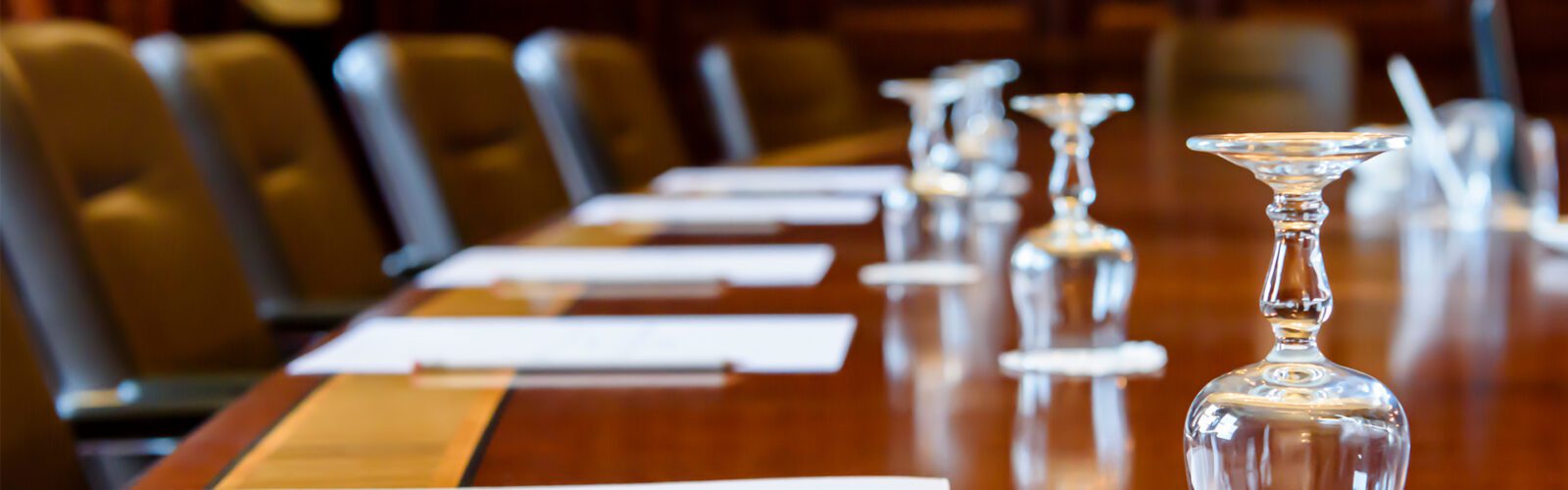 Large wooden table in a board room with wood panelling, set up for a meeting