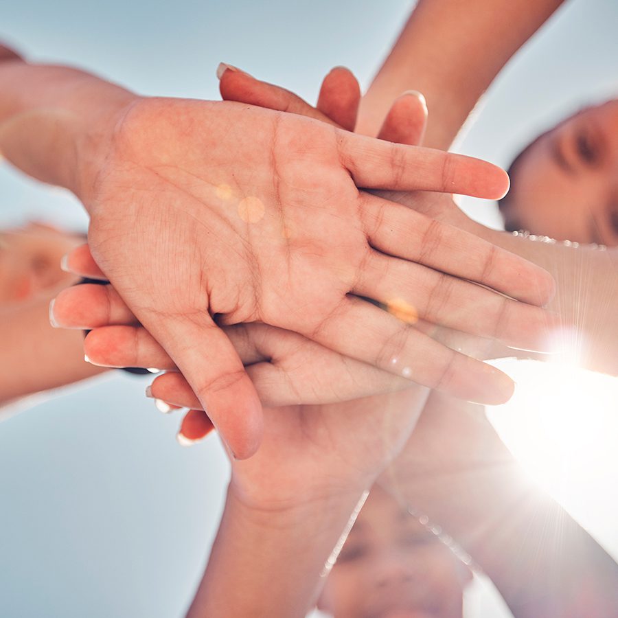 Hands, teamwork and collaboration of friends, community or people together for charity, support and motivation outdoor with lens flare. Group together for trust, commitment and synergy from below