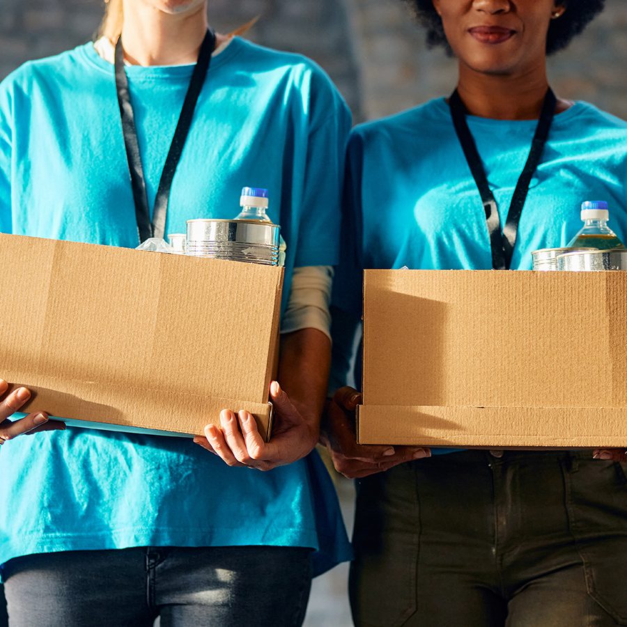 Unrecognizable volunteers carrying donation boxes at food bank. stock photo