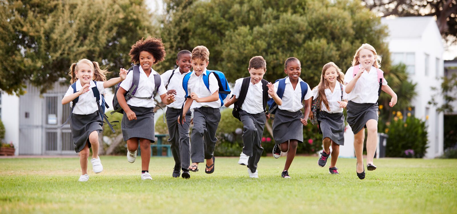 Excited Elementary School Pupils Wearing Uniform Running Across Field At Break Time