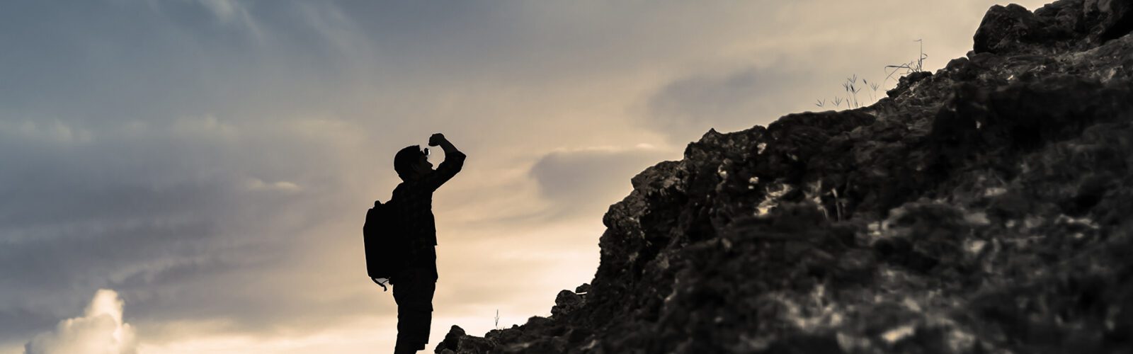 Man getting ready to climb up mountain looking up at the challenge before him planning path. Believe in yourself, overcoming challenges, pushing forward concept.