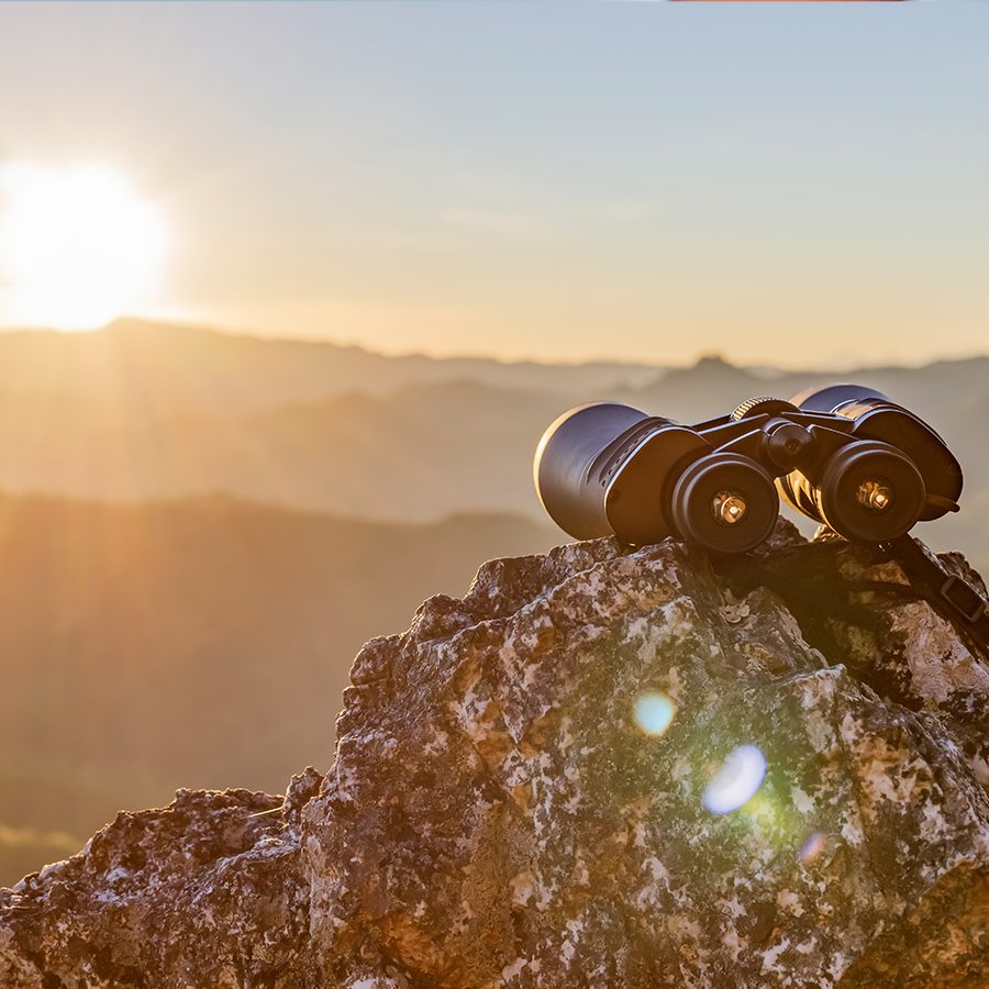 Binoculars on top of rock mountain at beautiful sunset background.